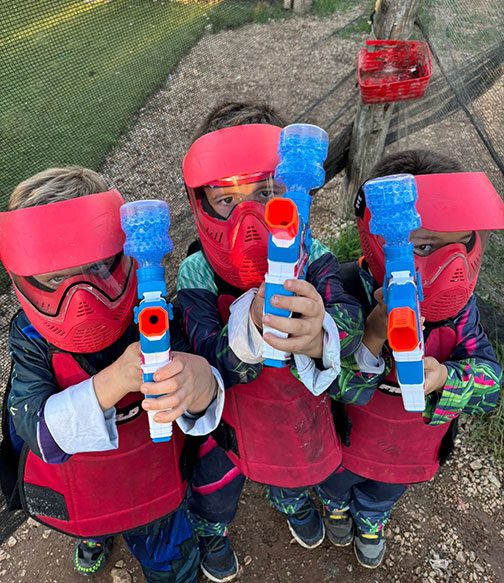 Niños jugando al paintball con equipación segura y adaptada